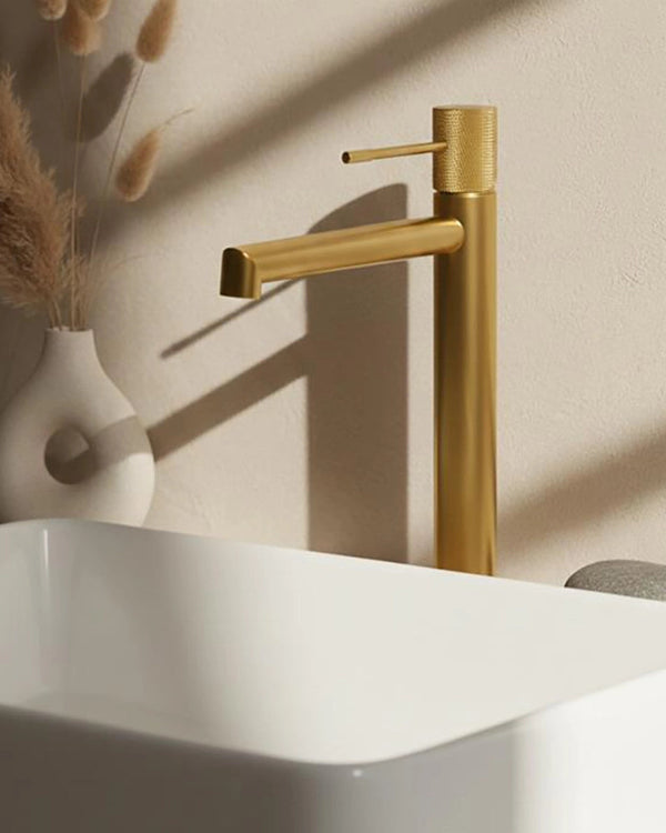 Rubinetto alto per lavabo senza scarico in ottone oro Oro Mat in spazzolato ambientato su piano bagno con accessori...