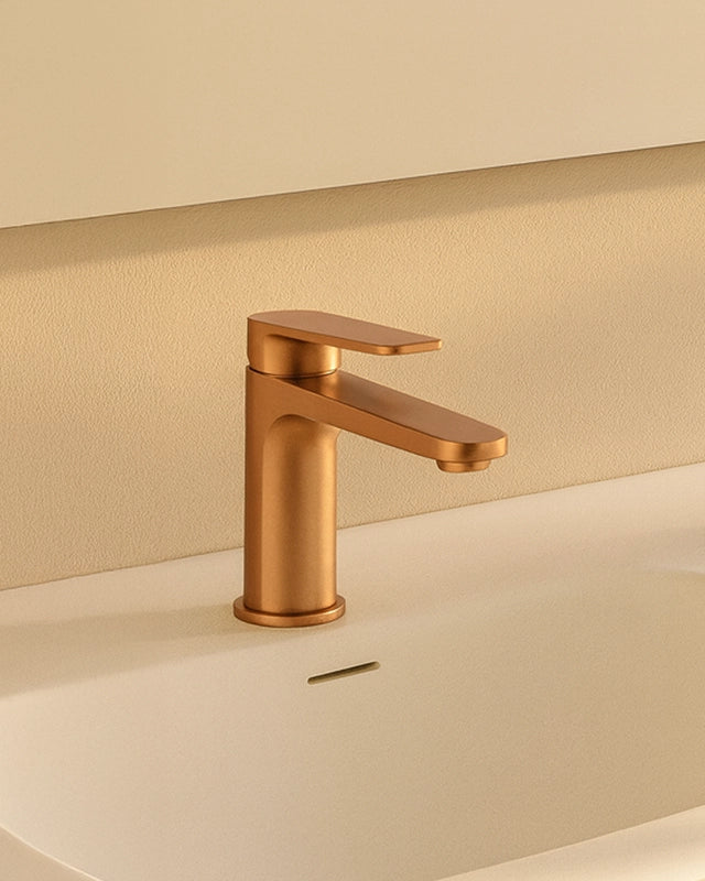 Miscelatore lavabo senza scarico in ottone oro rosa in spazzolato e naturale ambientato su piano bagno con accessori...