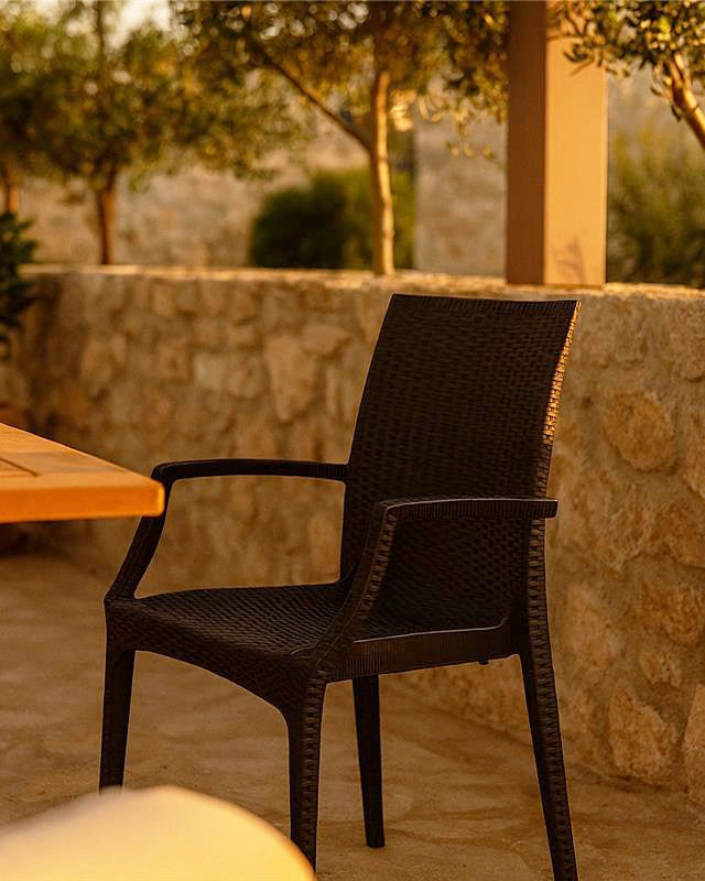 Sedia da esterno antracite effetto rattan con braccioli in naturale ambientato in spazio living con arredi coordinati...