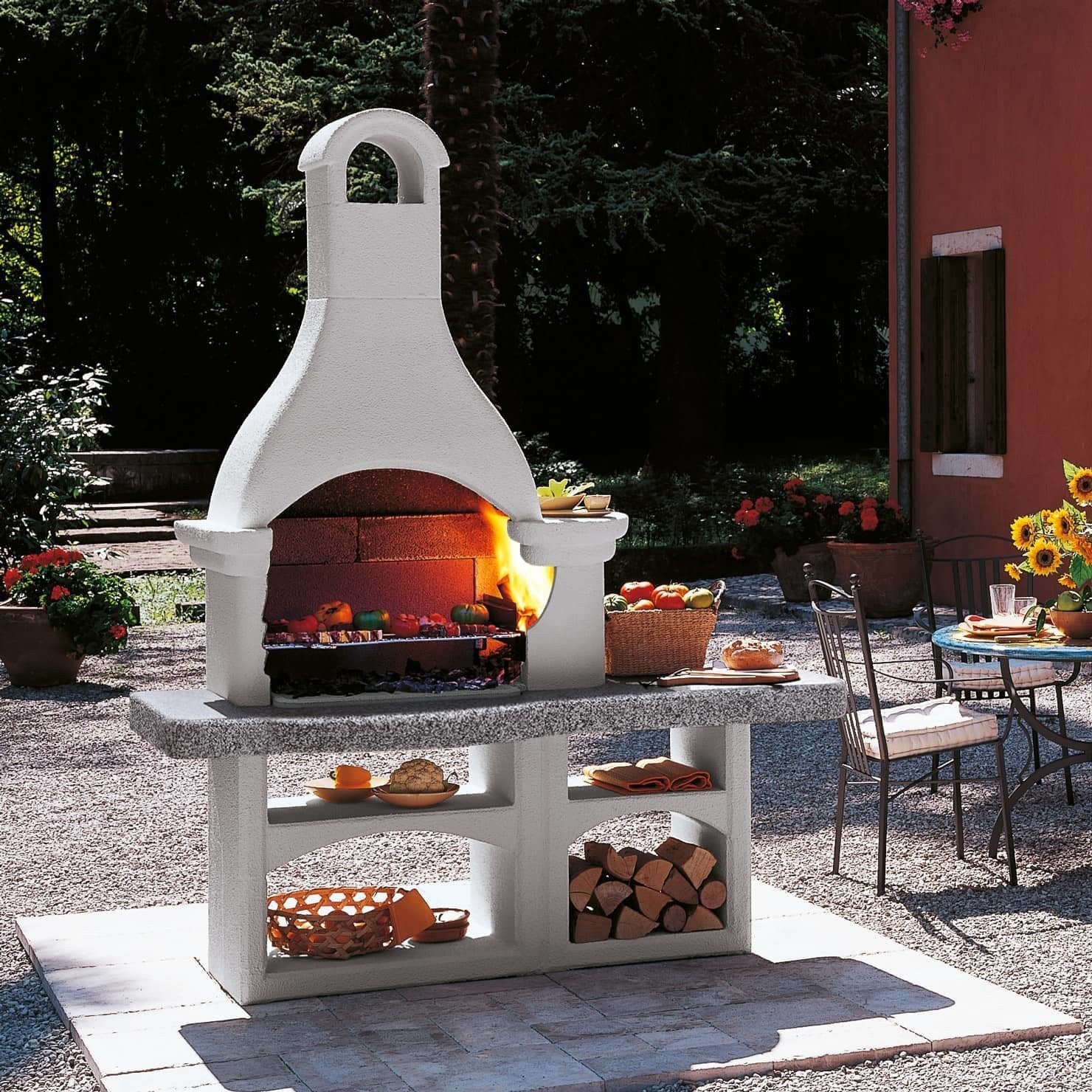 Palazzetti Lanzarote 3 barbecue grezzo con portalegna e accesa in soggiorno, fiamma visibile attraverso il vetro