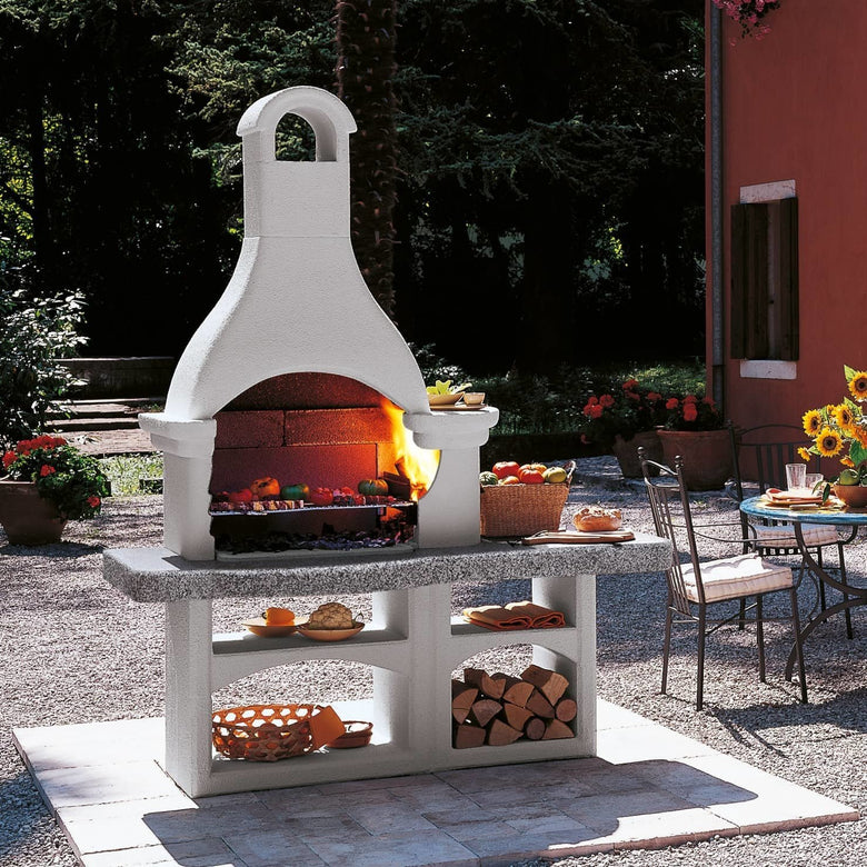 Palazzetti Lanzarote 3 barbecue grezzo con portalegna e accesa in soggiorno, fiamma visibile attraverso il vetro